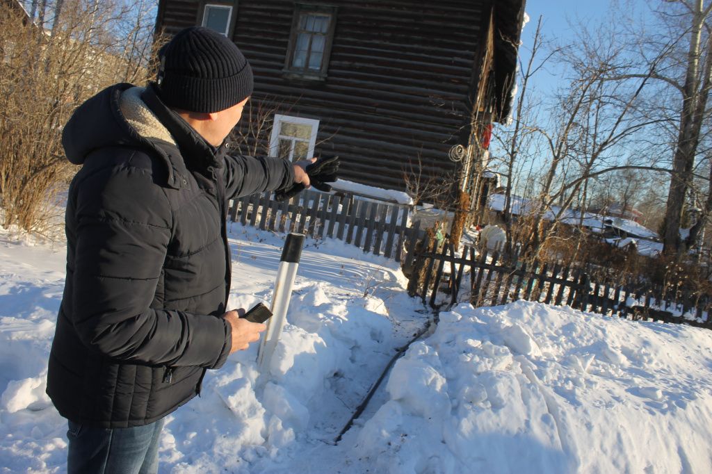 Александр Ильин показывает, что труба с холодной водой идет в дома №№3-а и 1-а. Если в одном из домов вода замерзает, то второй дом остается тоже без холодной воды. Фото: Мария Чекарова, "Глобус"